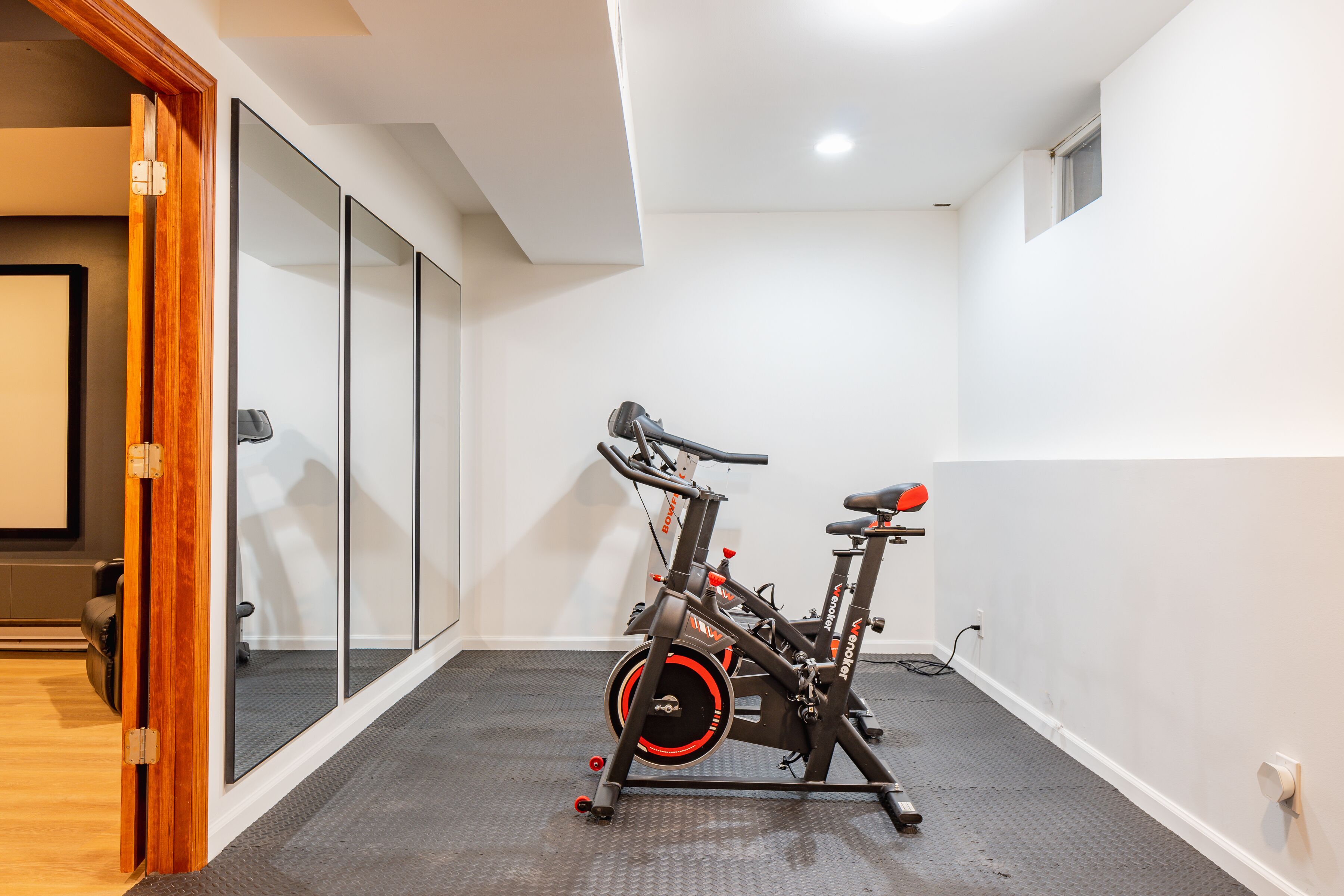 Una habitación pequeña con una bicicleta estática, una puerta que da a otra habitación y un ventanal.