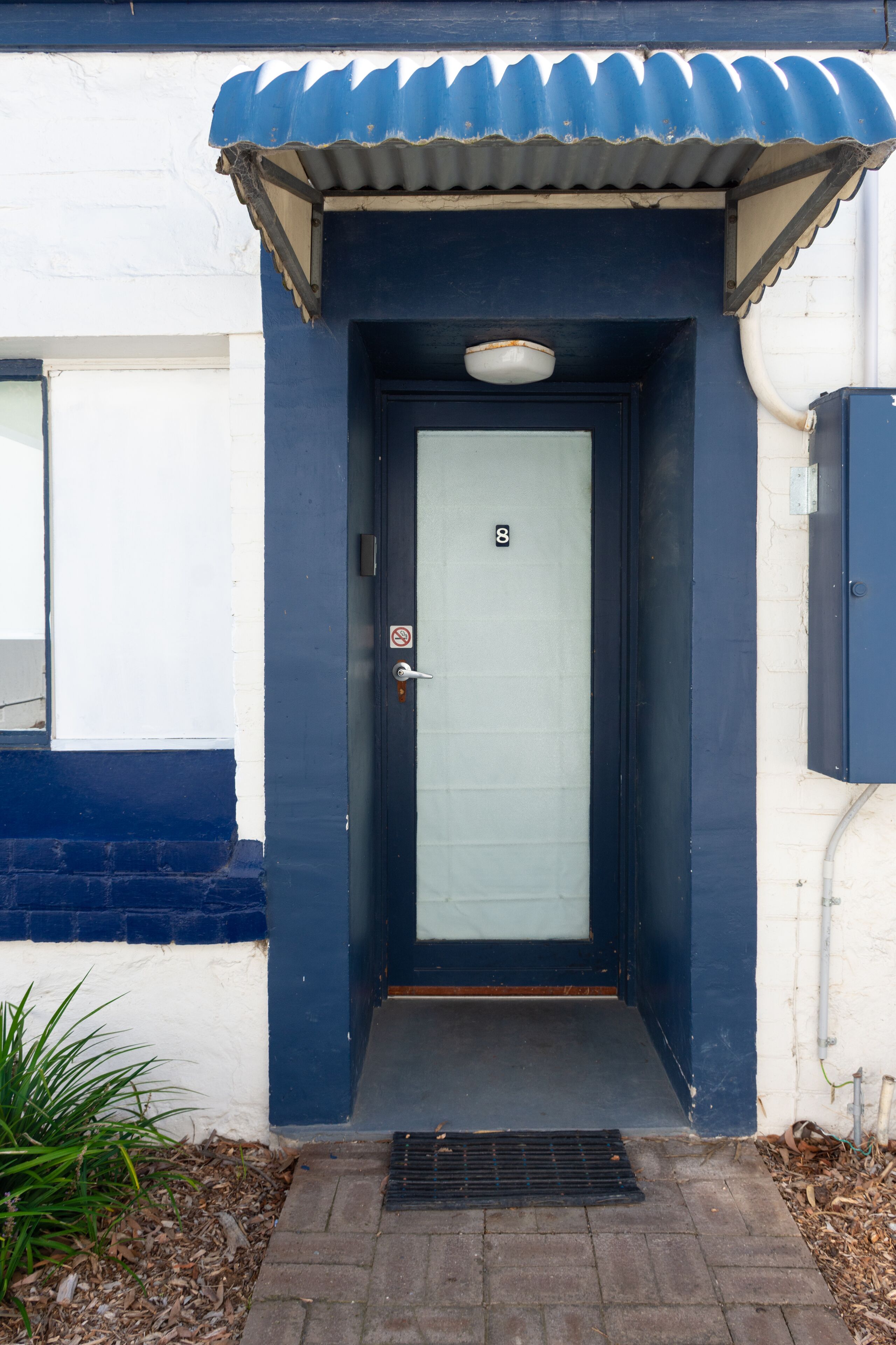 Una puerta azul oscuro con un panel blanco, una pequeña ventana a la izquierda y el número 8 sobre la puerta.