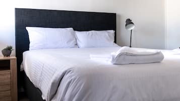 A neatly made bed with white linens, a dark headboard, and a bedside lamp.