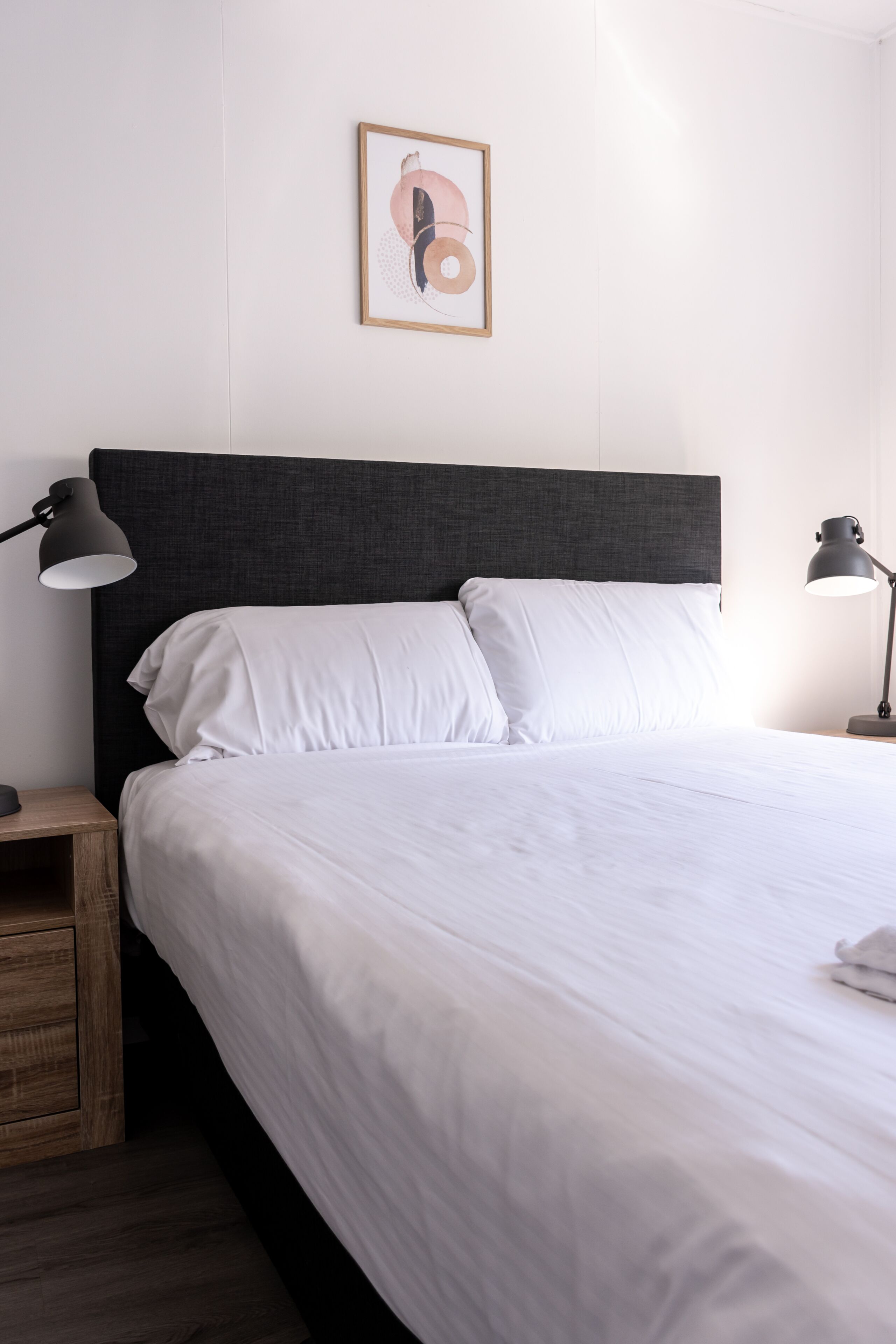 A neatly made bed with white linens, a dark headboard, and two bedside lamps.