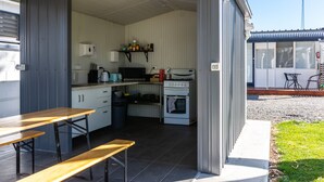 A compact kitchen with a microwave, stove, and a small refrigerator. There is a wooden bench outside the kitchen. - Motel on Becker (Tintinara)