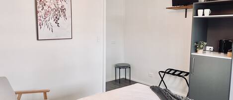 Habitación de hotel moderna con cama, una silla, un escritorio, televisor y repisa con tazas y una planta.