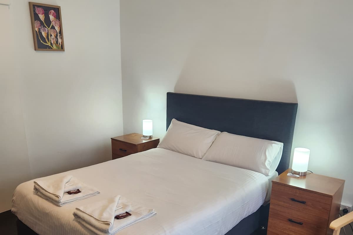 A neatly made bed with white linens, two bedside tables with lamps, and a small drawer.