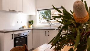A modern kitchen with white cabinets, a wooden dining table, and a window with a view of trees. - Motel on Becker (Tintinara)