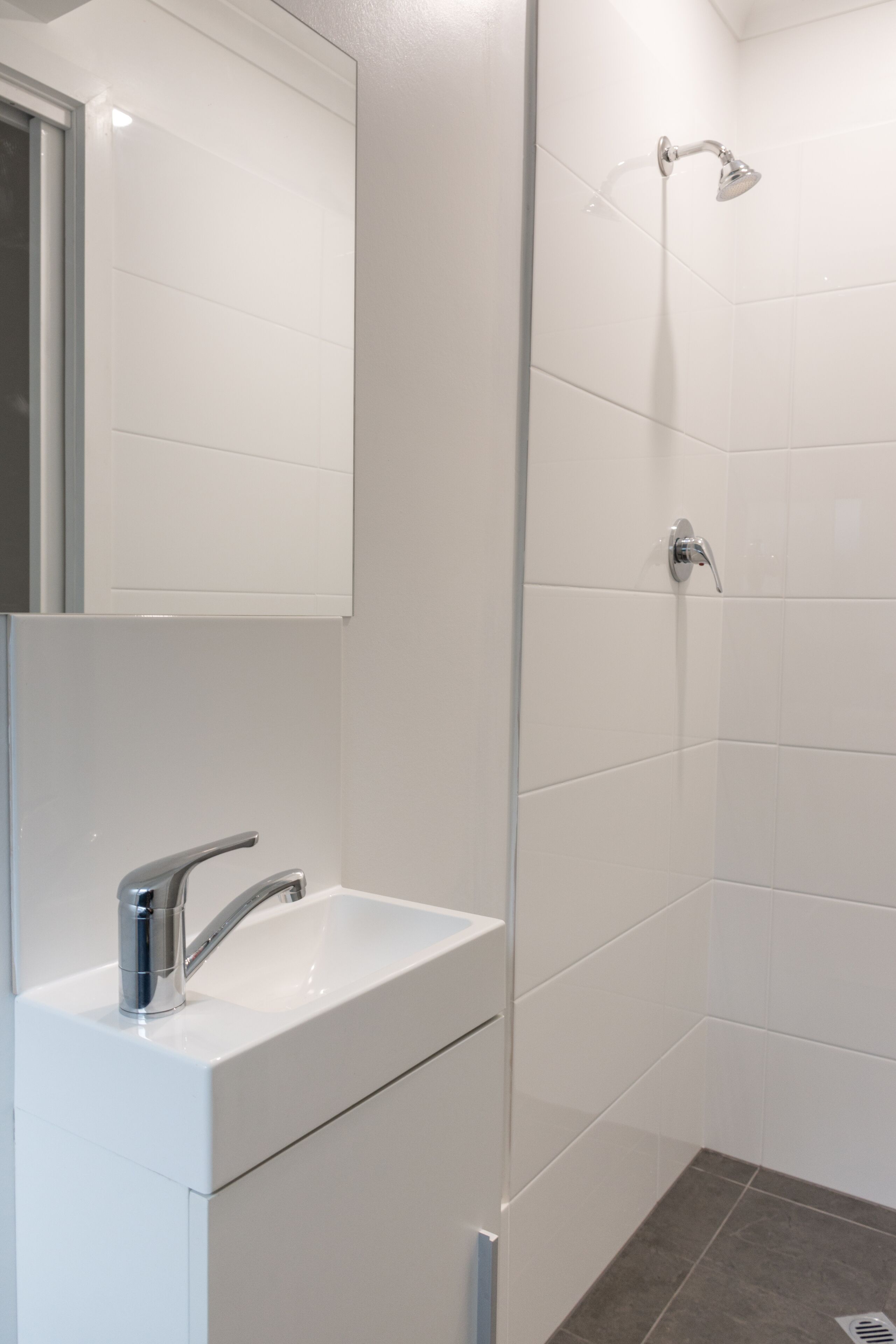 A modern bathroom with a white sink, a mirror, and a shower.
