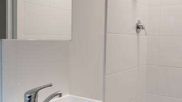 A modern bathroom with a white sink, a mirror, and a shower.
