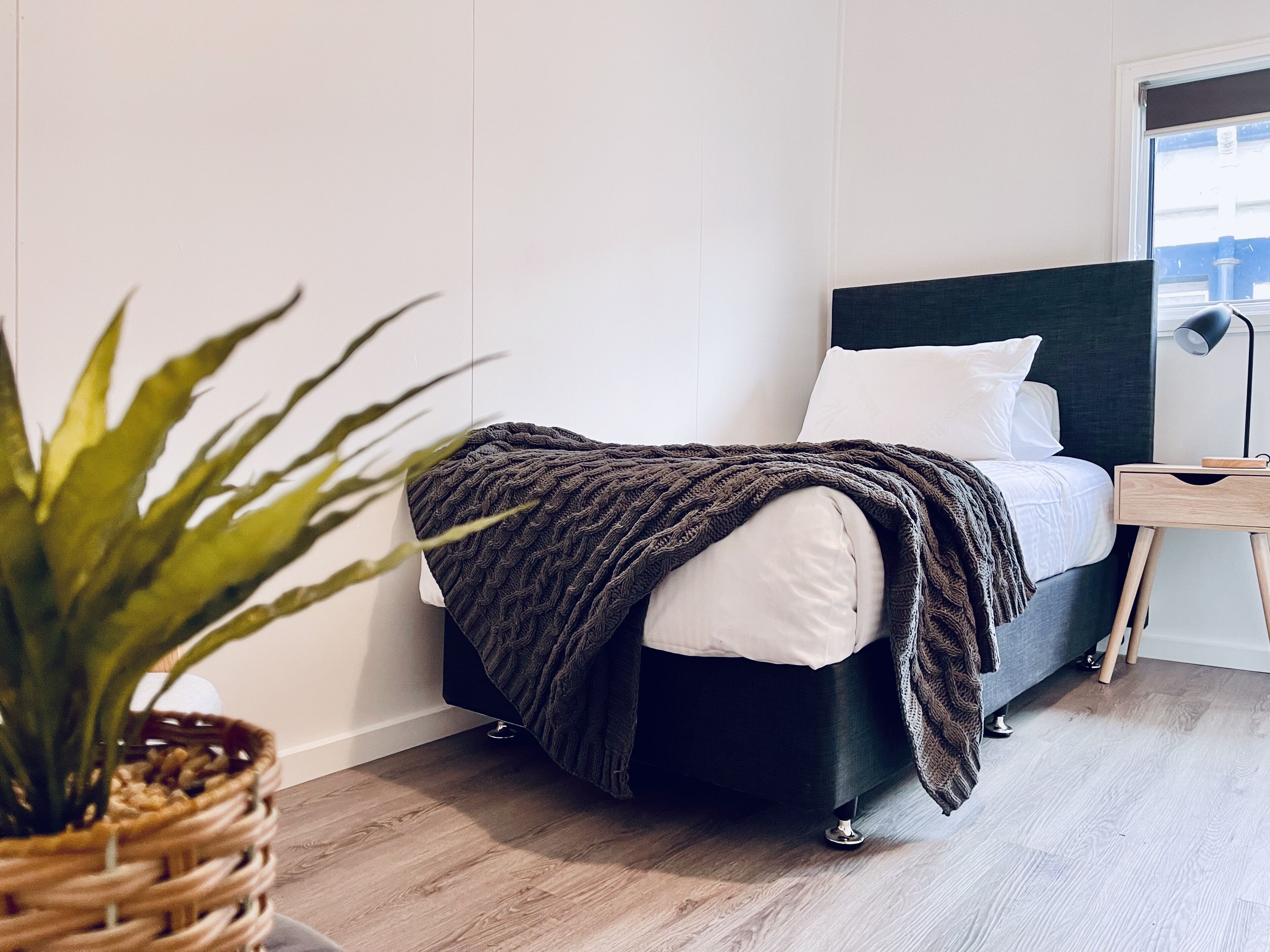 Un dormitorio moderno con cama, mesita de noche, lámpara y planta en maceta.