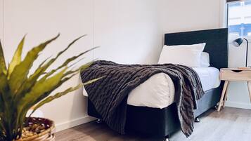 Un dormitorio moderno con cama, mesita de noche, lámpara y planta en maceta.
