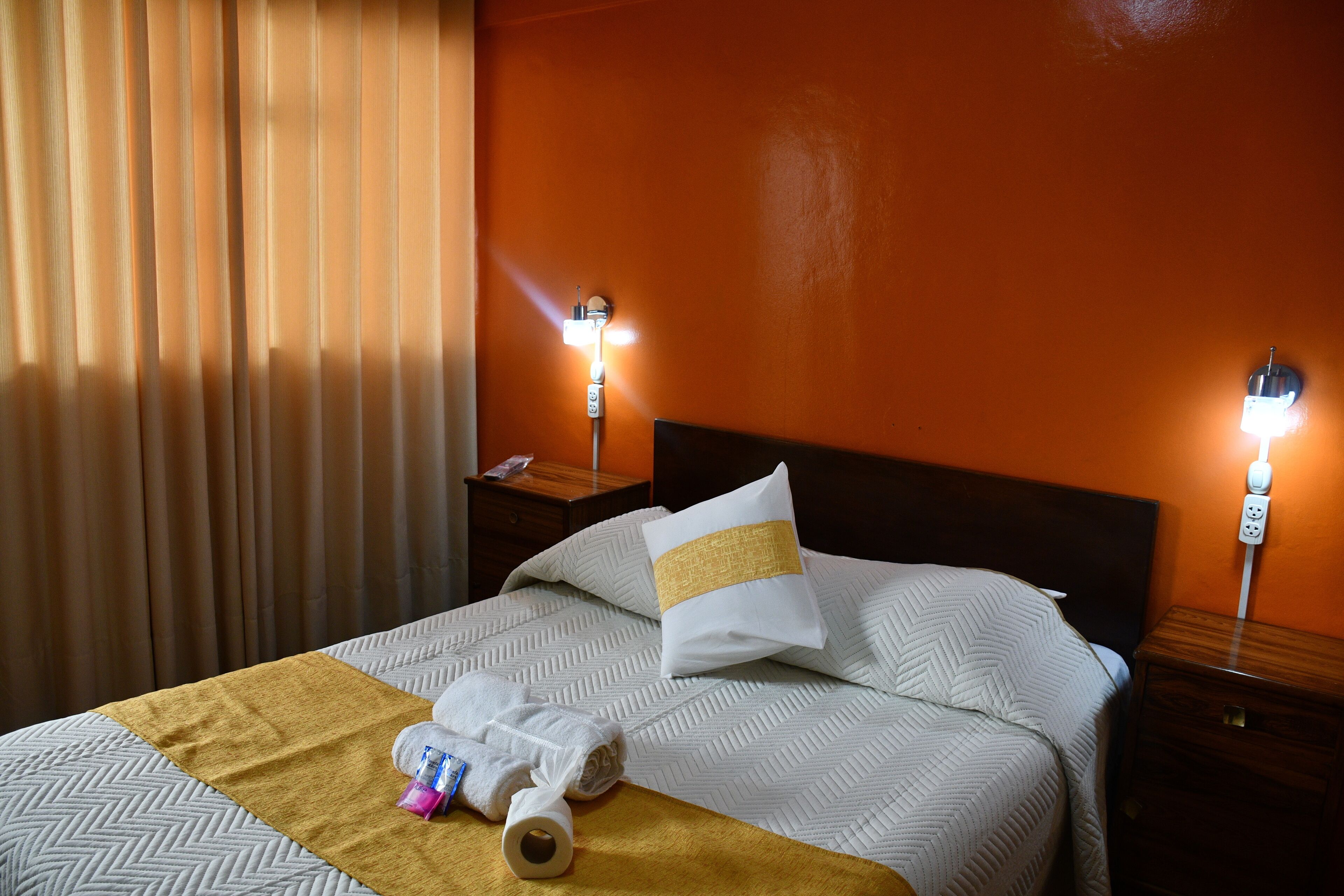 A neatly made bed with a patterned bedspread, a white pillow with a gold accent, and a brown throw blanket. There are two bedside lamps on the nightstands.