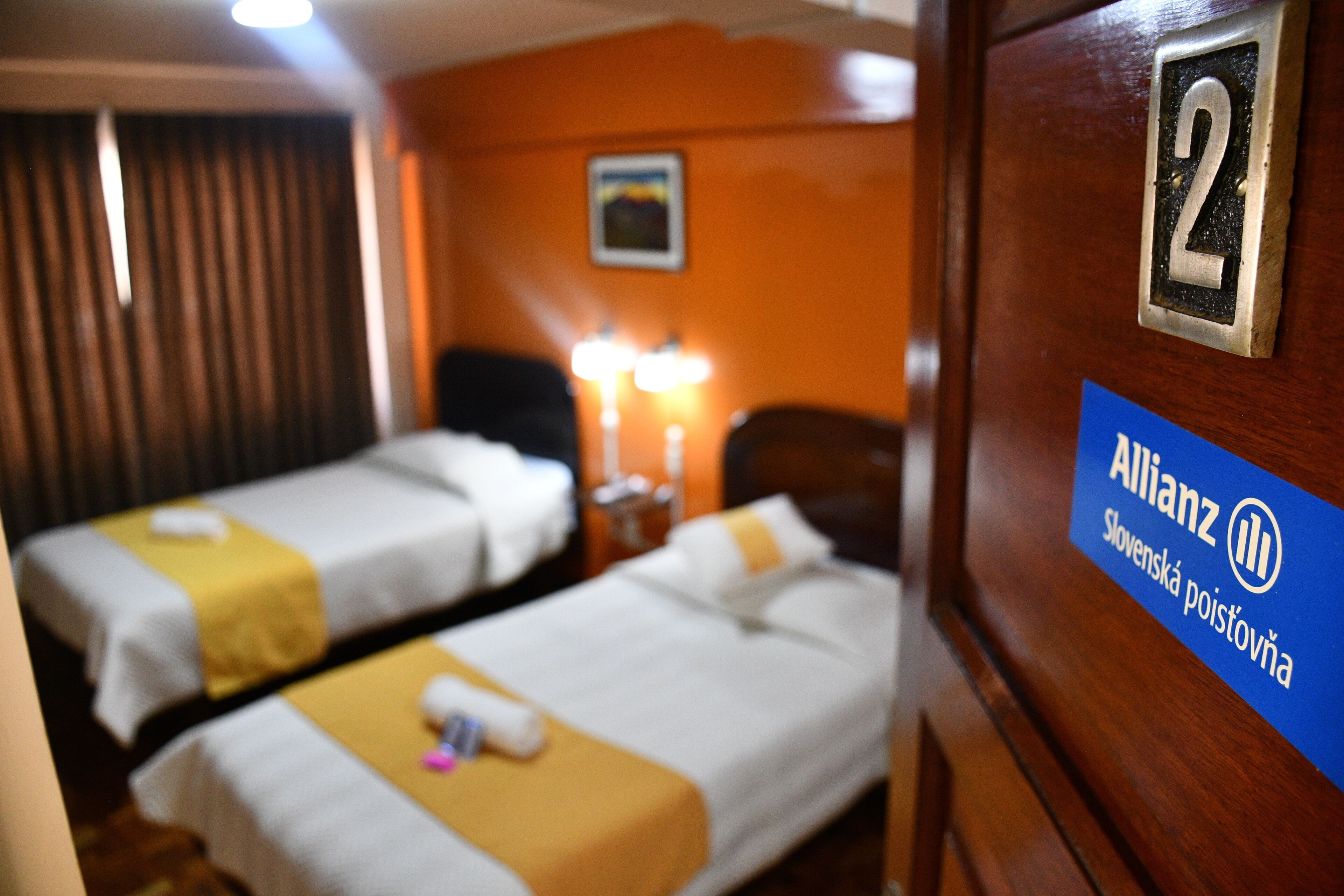A hotel room with two beds, a nightstand, and a sign indicating room number 2.