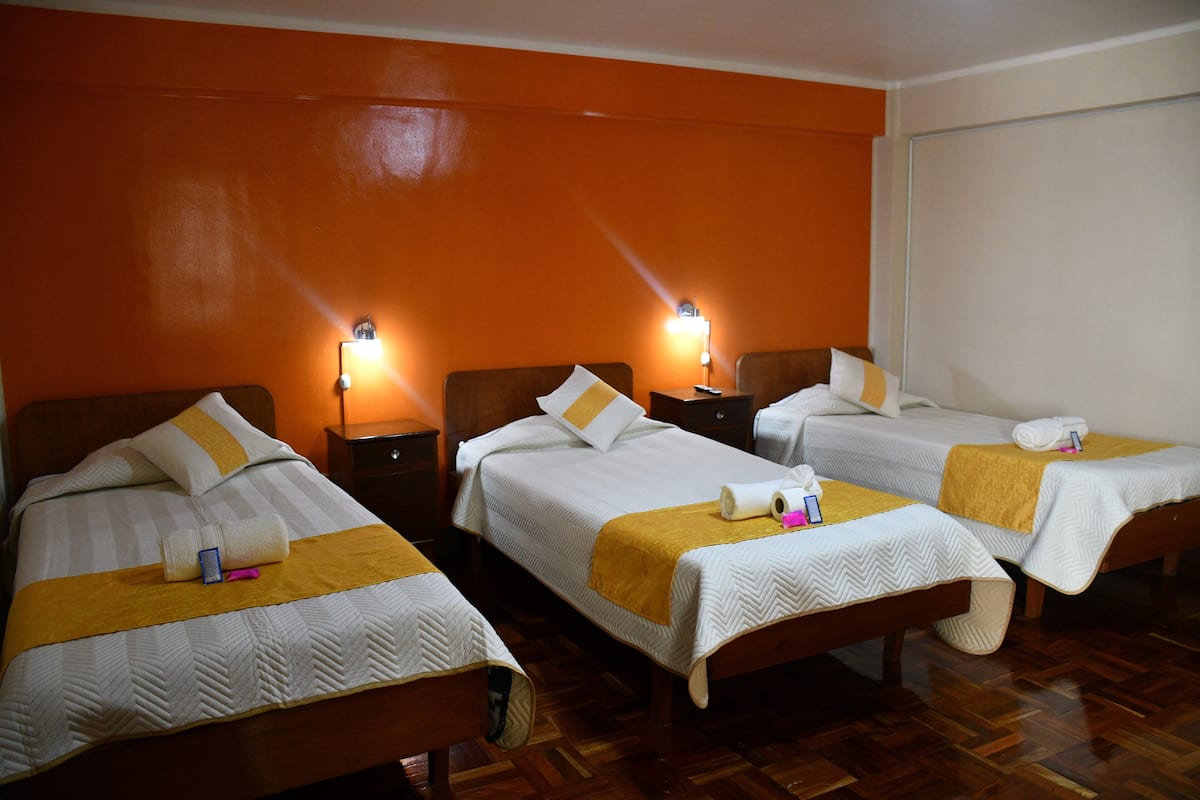 A hotel room with three single beds, wooden headboards, and bedside lamps.