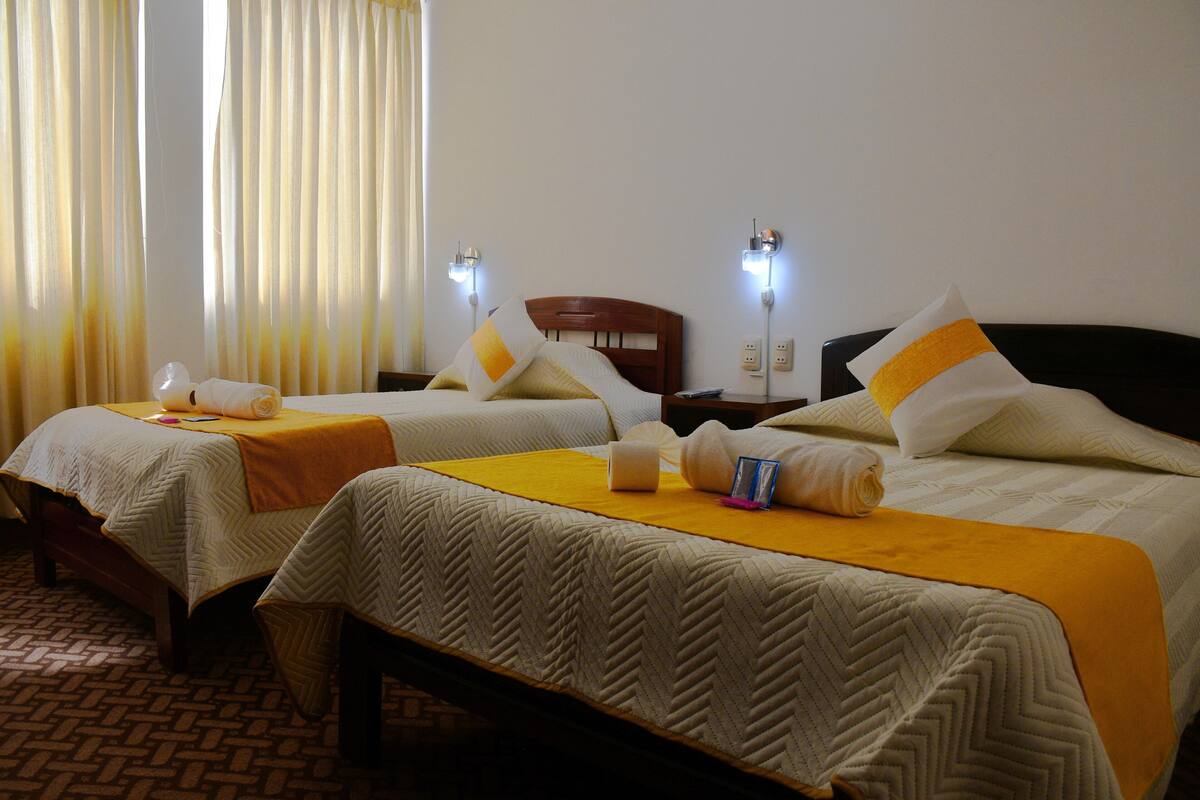 A hotel room with two beds, each with a yellow bedspread and white pillows. There are two bedside lamps and a wooden headboard.