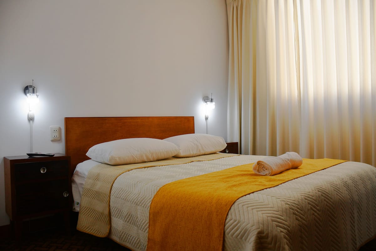 A neatly made bed with a wooden headboard, two bedside tables with lamps, and a window with curtains.