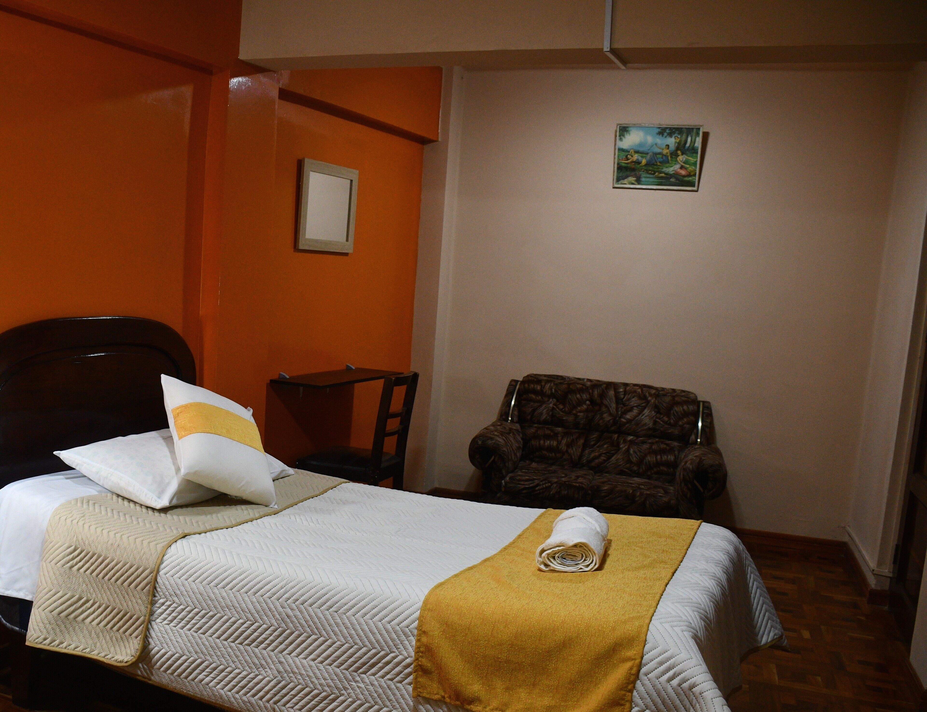 A hotel room with a bed, a chair, a small table, and a painting on the wall.