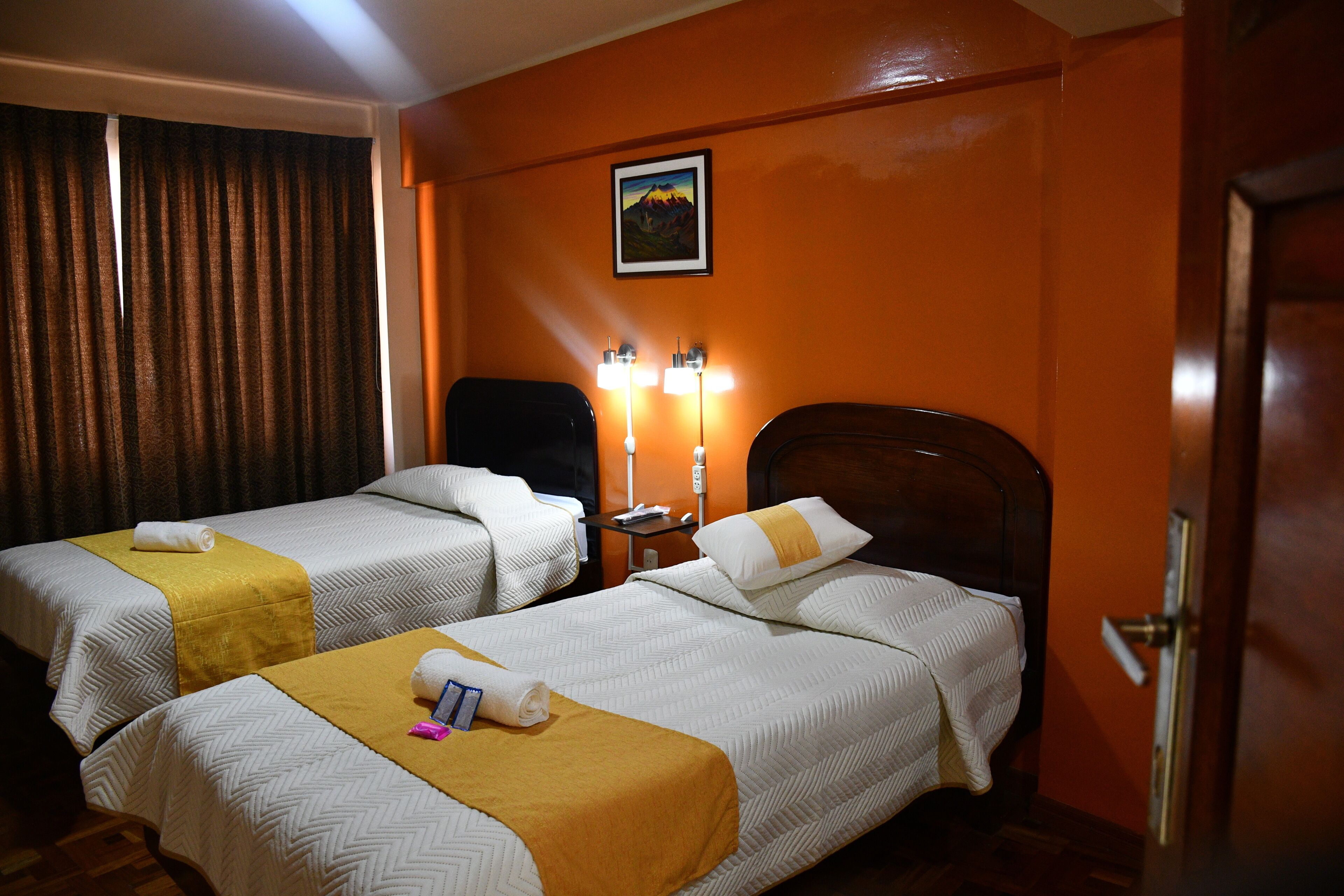A hotel room with two beds, a nightstand, a lamp, and a door.