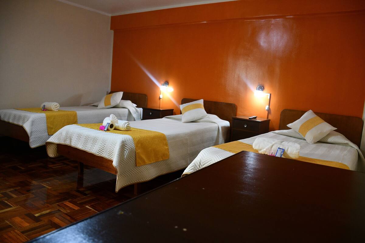 A hotel room with three beds, wooden flooring, and two bedside lamps.