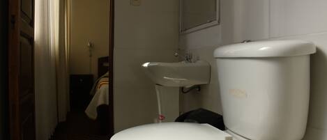 Un baño con inodoro blanco, lavamanos y espejo.