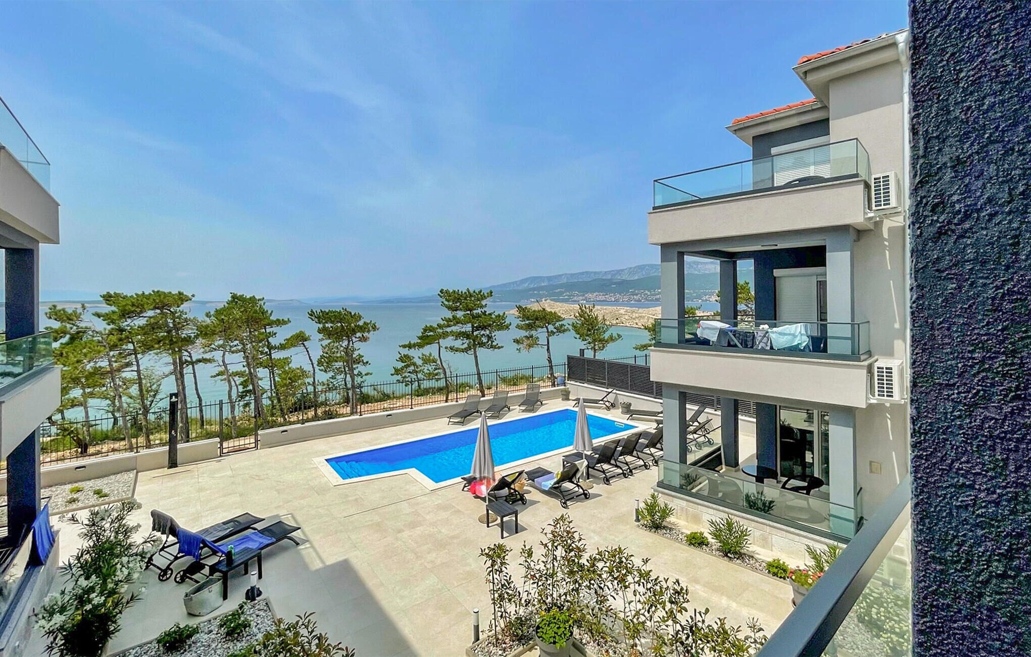 Um edifício moderno com piscina no terraço, espreguiçadeiras e vista para o mar.