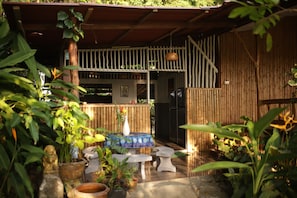 A covered outdoor area with a table and chairs, surrounded by potted plants and a bamboo fence. - The Source Koh Phangan (Ko Pha-ngan)