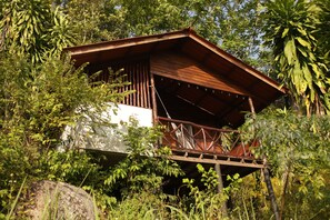 A wooden cabin with a balcony, surrounded by dense foliage. - The Source Koh Phangan (Ko Pha-ngan)