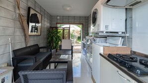 Cocina compacta con estufa a gas, horno empotrado y microondas. Hay un comedor con mesa y sillas, y un pequeño rincón de estar con sofá y mesa de centro.