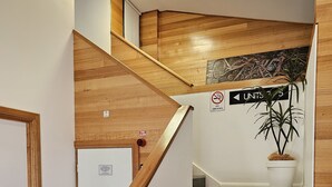 A modern staircase with wooden handrails and grey steps, leading to a landing with a 'No Smoking' sign and a 'Fire Alarm' sign.