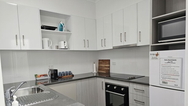 A modern kitchen with white cabinets, a stainless steel sink, a built-in oven, and a microwave.