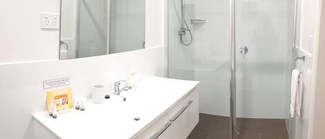 A modern bathroom with a white vanity, a glass shower enclosure, and a large mirror.