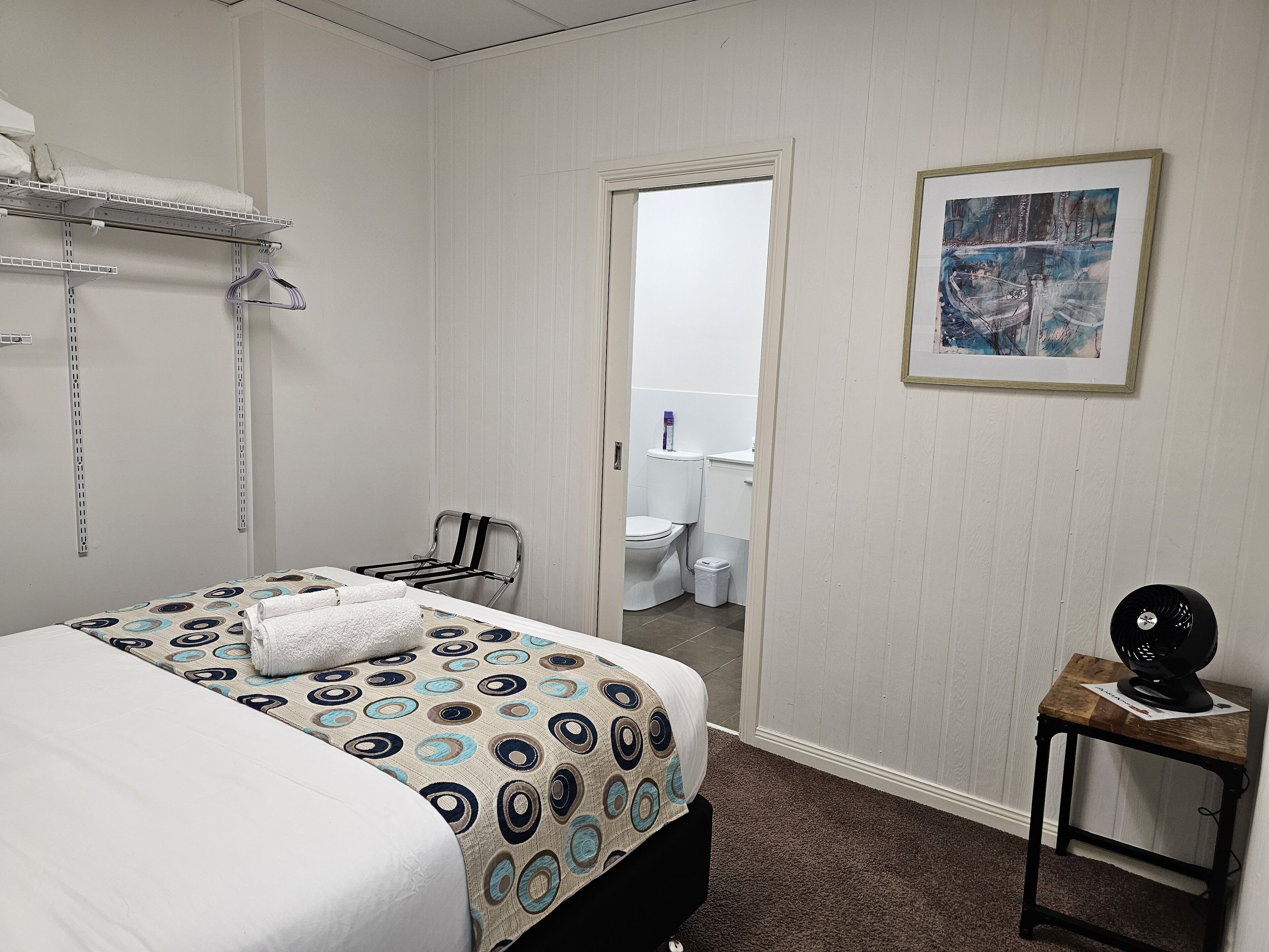 Habitación de hotel con cama, una silla, una mesita, un espejo y un cuadro en la pared.