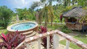 A hot tub in a lush garden with a thatched-roof structure nearby. - Kalipay Bungalows (Alcoy)