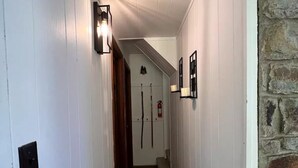 A narrow hallway with white walls, wooden flooring, and a stone wall on the right. There are light fixtures on the walls and a fire extinguisher mounted on the wall. - 4 min Beech Mtn. Gem: Cabin Retreat near Slopes & Trails 
Pet friendly (Beech Mountain)
