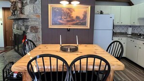 A dining area with a wooden table and four black chairs, a stone fireplace, and a framed landscape painting above the table. - 4 min Beech Mtn. Gem: Cabin Retreat near Slopes & Trails 
Pet friendly (Beech Mountain)