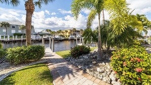 A marina with boats docked, surrounded by palm trees and a pathway leading to a building. - Punta Gorda 3-Bedroom Canalfront Vacation Condo with Dock (Punta Gorda)