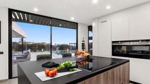 A modern kitchen with a large island, a built-in oven, and a view of a swimming pool. - KARAT Villa Serendibida (Playa Paraiso)