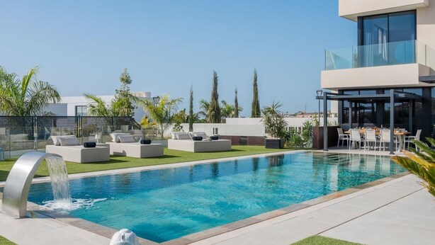 A modern outdoor pool area with a clear blue pool, lounge chairs, and a waterfall feature. - KARAT Villa Serendibida (Playa Paraiso)