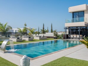 A modern outdoor pool area with a clear blue pool, lounge chairs, and a waterfall feature. - KARAT Villa Serendibida (Playa Paraiso)