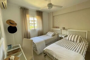 A hotel room with two beds, a ceiling fan, a window with curtains, a radiator, and a small table with a lamp. - Townhouse Terrace with sea view close to Marbella (Calahonda)