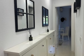 Um corredor com um console branco, dois espelhos com moldura preta e um pequeno vaso preto com raminhos.