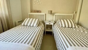 A twin room with two beds, each with striped bedding, a small bedside table with a lamp, and a decorative wall piece.