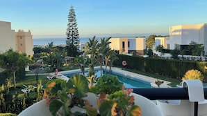A pool area with a view of the sea, surrounded by modern buildings and greenery.