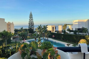 Área da piscina com vista para o mar, rodeada por edifícios modernos e vegetação.