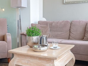 Un salon avec une table basse en bois, une plante en pot, une bouilloire et un verre d’eau.