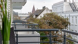 A balcony with metal railings overlooking a row of buildings with traditional architecture, including a church steeple. - Meeresrauschen - Haus Dünenburg, Elisabethstraße 9 - Diese Freundlich Eingerichtete 2-zimmer-wohnung (Westerland)