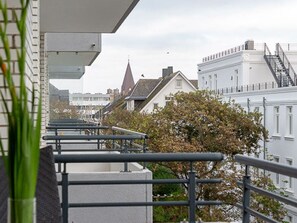 A balcony with metal railings overlooking a row of buildings with traditional architecture, including a church steeple. - Meeresrauschen - Haus Dünenburg, Elisabethstraße 9 - Diese Freundlich Eingerichtete 2-zimmer-wohnung (Westerland)