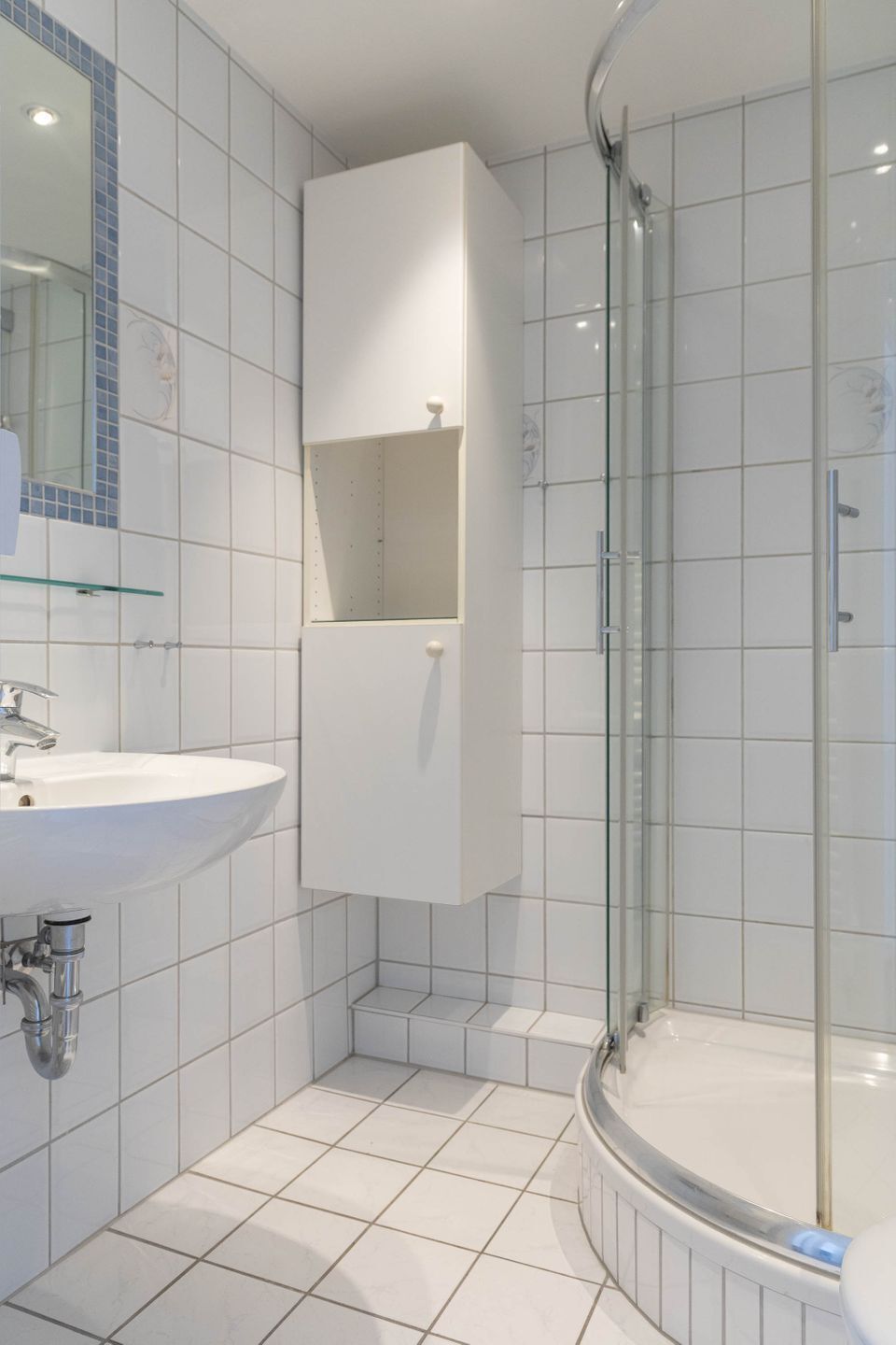 Ein Badezimmer mit einem weißen Waschbecken, einer Duschkabine aus Glas und einem weißen Schrank.