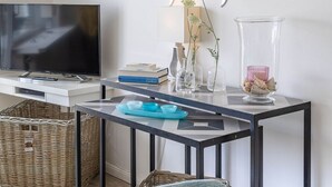 Ein modernes Wohnzimmer mit Flachbildfernseher, einem Esstisch mit Stühlen, Wandkunst und einer Vase mit Blumen.
