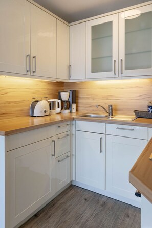 A modern kitchen with white cabinets, a wooden countertop, a coffee maker, and a sink. - Meeresrauschen - Haus Dünenburg, Elisabethstraße 9 - Diese Freundlich Eingerichtete 2-zimmer-wohnung (Westerland)