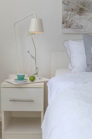 Une table de chevet blanche, avec une lampe, un petit bol et une pomme verte.