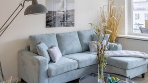 Ein modernes Wohnzimmer mit einem grauen Sofa, einem runden Couchtisch und einer Pendelleuchte.