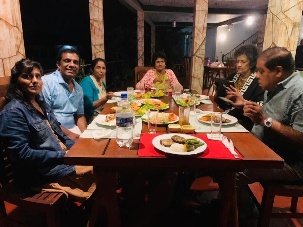 A group of people seated around a wooden dining table with various dishes and drinks.